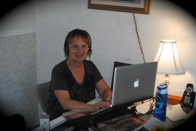 English tutor Mary Graydon is sitting at her desk and computer with her headset on.